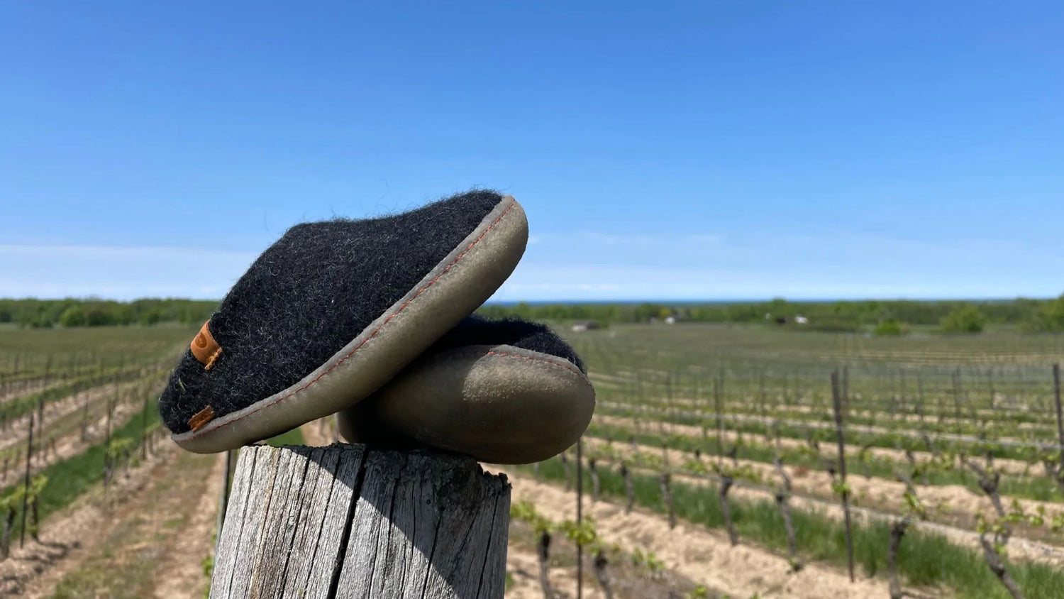 A pair of Betterfelt Classic Slippers in Back with Rubber Soles Perched On A Fence Post